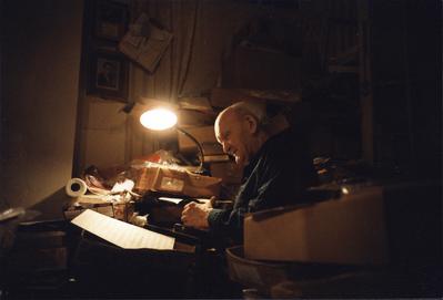 Bill Russell, half length portrait, seated, facing slightly left, lit by a  lamp surrounded by papers in boxes, New Orleans LA., (1982)