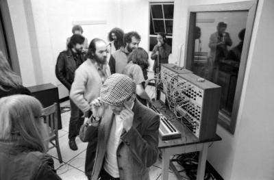 Tom Zahuranec  looks on as a person adjust settings on synthesizer, at a KPFA Radio Event, Mills College, Oakland CA, 1971