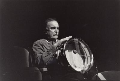Alvin Lucier, half length portrait, seated, facing slightly right and holding instrument, (1999)