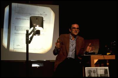David Rosenboom seated onstage, with overhead projector at the Exploratorium