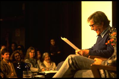 John Cage, seated onstage, reading during an appearance at the Exploratorium, 1987