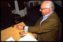 David Raksin, seated at a table feeding a Frito to a dog, Exploratorium