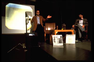 David Rosenboom, standing, and Charles Amirkhanian seated onstage during Speaking of Music at the Exploratorium, San Francisco (1986)