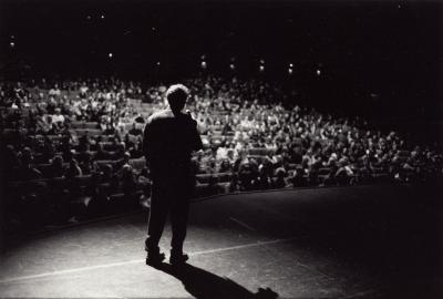 Charles Amirkhanian, full length portrait, standing, with back to camera and facing the audience of OM 8, San Francisco CA, (2002)
