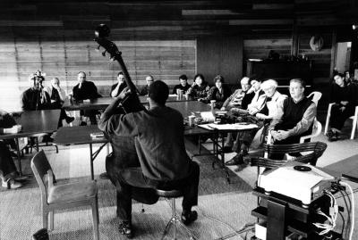 Alex Blake, full length portrait, seated, back to camera, showing off bass to fellow OM 10 participants, Woodside CA, (2004)