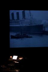 Michael Nyman, seated at piano, back to camera, with an image of ships projected above him, vertical ver. San Francisco CA., (2005)