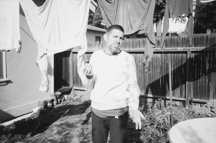 Anthony Gnazzo, three quarter length portrait, standing in a backyard, facing forward, holding a fig, Oakland CA., (1982)