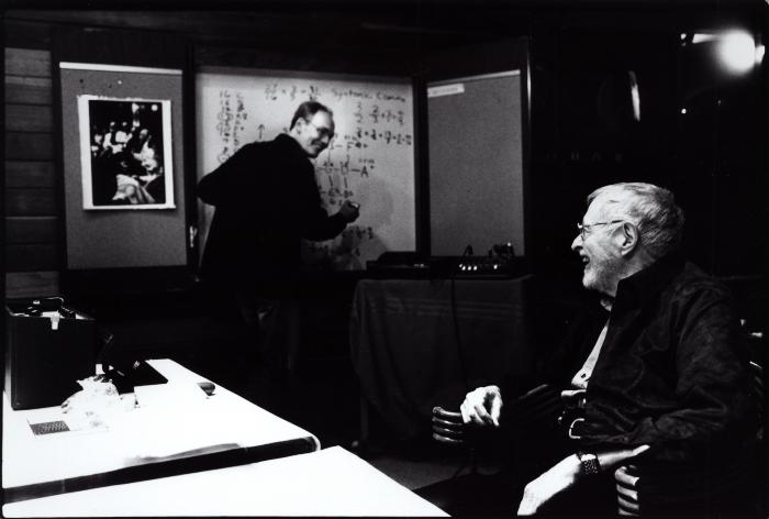 Michael Harrison, standing and Ben Johnston, seated (l to r), facing each other and smiling, Woodside CA, (2009)