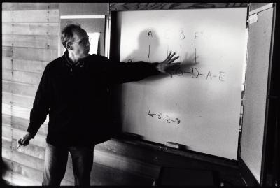 Michael Harrison, three quarter length portrait, standing, looking and pointing at notes on a white board, ver. 2, Woodside (cropped image)
