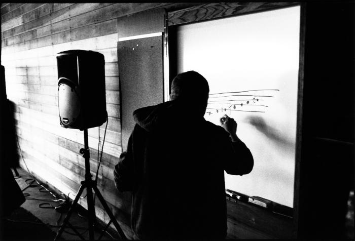Paweł Mykietyn, head and shoulders portrait, back to camera, writing on whiteboard, Woodside (cropped image)