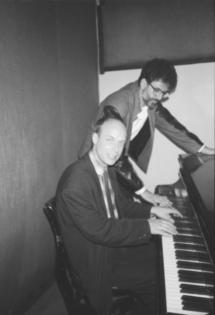 Charles Amirkhanian standing next to the KPFA piano with Brian Eno (seated), 1988