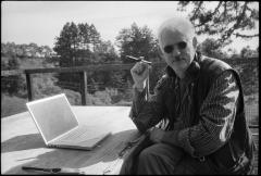 Half length portrait of Kyle Gann, seated outdoors with a laptop and cigar, Woodside CA (2011)