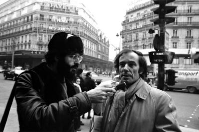 Heads and shoulders portrait of Charles Amirkhanian (with microphone) interviewing Bernard Heidsieck on street in Paris, 1973