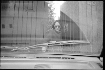 Yoko Sugiura Nancarrow, standing in front of a gate, as seen through the windshield of a car, Mexico, 1990