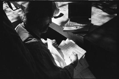 Trimpin, over the shoulders shot, seated, looking down to right, examining score, 1993