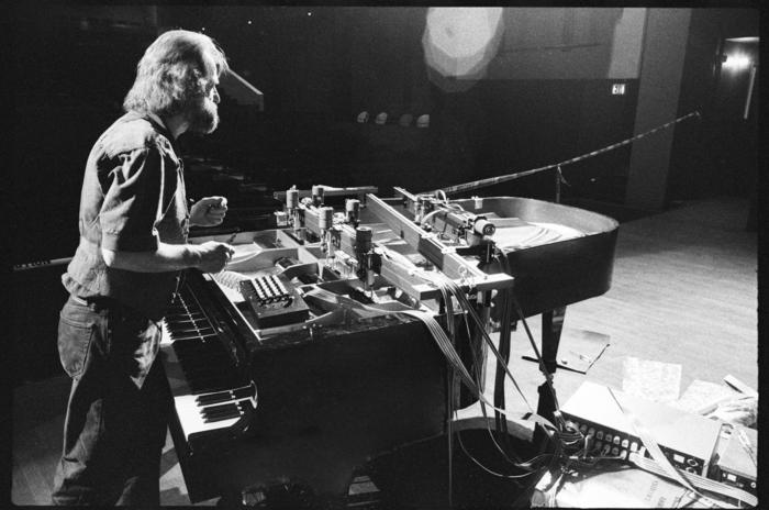 Trimpin, three quarter length portrait, standing over a piano, 1993