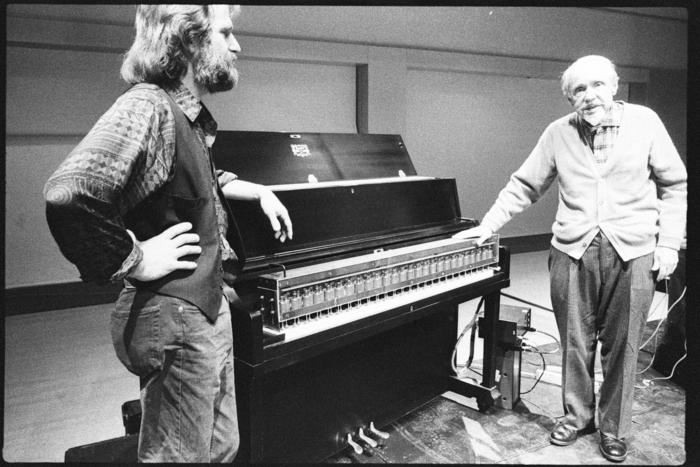 Trimpin, facing right, and Conlon Nancarrow, facing camera,standing, flanking a modified piano, (1993)