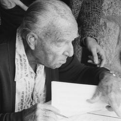 Ernst Krenek, seated, head and shoulders portrait, pointing over page of a score (1985)