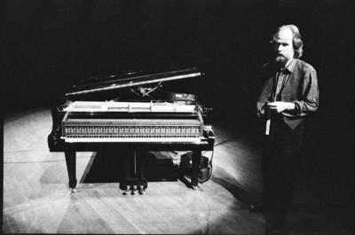 Trimpin, full length portrait, standing next to a modified piano, 1993