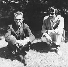George Oppen and Charles Hanzlicek smiling, sitting on the grass outside the Arena Theater in Fresno, CA (1967)