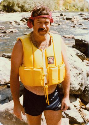 Portrait of artist John White, wearing a life vest, standing by the bank of the Klamath River, 1981