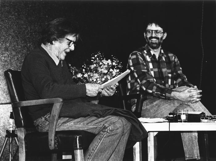 John Cage & Charles Amirkhanian (l to r), full length portrait, seated on stage, San Francisco CA., (1987)