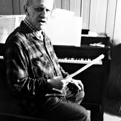 Leo Ornstein, seated at piano, facing forward, holding musical score, Brownsville TX, 1981