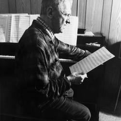 Leo Ornstein, seated at piano, leaning slightly forward, facing right, looking at a musical score, Brownsville TX, 1981