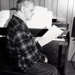 Leo Ornstein, seated at piano, facing right, looking at a musical score, Brownsville TX, 1981