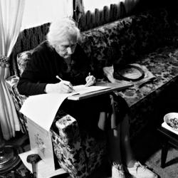 Pauline Ornstein seated on a couch examining a document, Brownsville TX, 1981