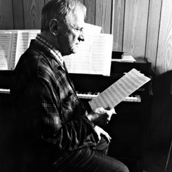 Leo Ornstein, seated on piano bench, facing right, looking at musical score, Brownsville TX, 1981