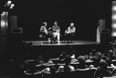 John Cage, Charles Amirkhanian, and Conlon Nancarrow in conversation on stage, with audience in the foreground, Telluride, CO. (1989)