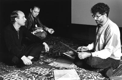 Brian Eno, Anthea Norman-Taylor, and Charles Amirkhanian seated on the floor reviewing slides and albums, 1988