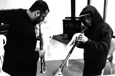 Hafez Modirzadeh and Henry Brant, half length portrait, facing each other playing horns, Woodside CA (1997)