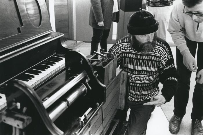 Rex Lawson, three quarter length portrait, facing down and to the right, pointing to his pianola, (1995)