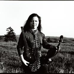 Mari Kimura, three quarter length portrait, kneeling in field holding her violins, facing forward, Woodside CA, (1995)