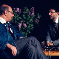 A three quarter length portrait of Mauricio Kagel and Charles Amirkhanian seated onstage in discussion during Speaking of Music at the Exploratorium, San Francisco (1988)