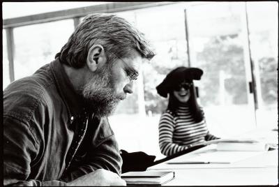 Head and shoulders portrait of Charles Shere reading, while Kui Dong smiles in the background, Woodside, CA (1996)