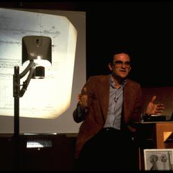 David Rosenboom seated onstage, with overhead projector at the Exploratorium