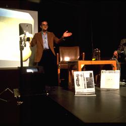 David Rosenboom, standing, and Charles Amirkhanian seated onstage during Speaking of Music at the Exploratorium, San Francisco (1986)