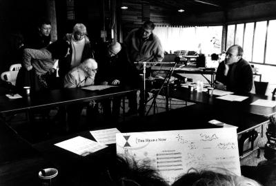 OM 10 participants examine a score by Jon Raskin, standing and seated around conference table, Woodside, 2004