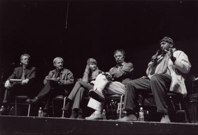 William Parker speaking, seated onstage with other guests during an artist's forum for OM 9, San Francisco (cropped image)