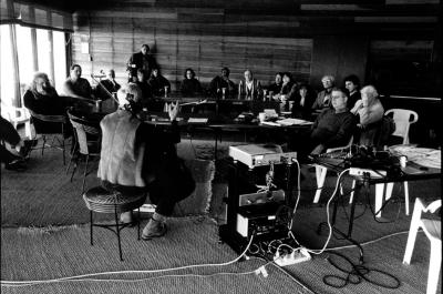 Joan Jeanrenaud, seated, back to camera, demonstrates cello to OM 10 participants, who are seated at conference table, facing forward, Woodside