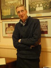 Alden Jenks, standing in front of a wall with framed photographs (2011)