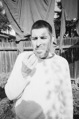 Anthony Gnazzo, half length portrait, standing in a backyard, facing forward, eating a fig, Oakland CA., (1982)