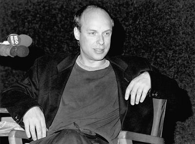Brian Eno, seated onstage during Speaking of Music at the Exploratorium, 1988