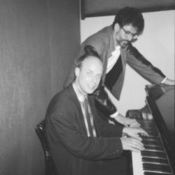 Charles Amirkhanian standing next to the KPFA piano with Brian Eno (seated), 1988