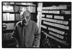 Conlon Nancarrow, wearing glasses, standing in front of shelves of books and player piano rolls, Mexico, 1990