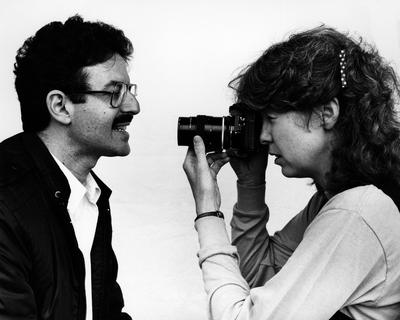 Charles Amirkhanian smiles as Carol Law points a camera at his mouth, Oct. 1983