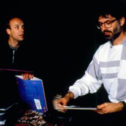 Brian Eno and Charles Amirkhanian seated on the floor reviewing albums, 1988